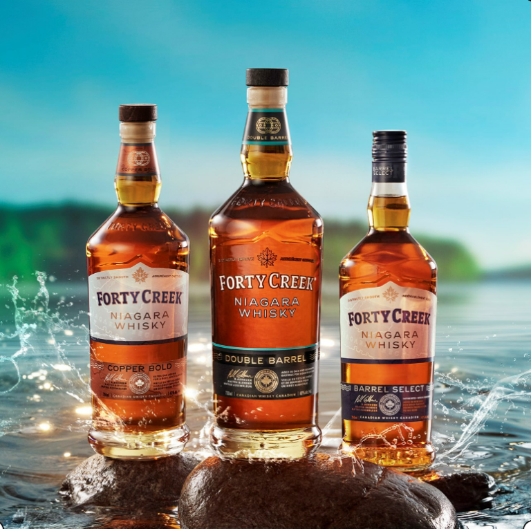 Three bottles of Forty Creek Whisky sit on a rock around splashing waves.