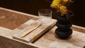 Wooden toothbrush with rippled water glass set on high-end marble countertop with a vase of fresh flowers.