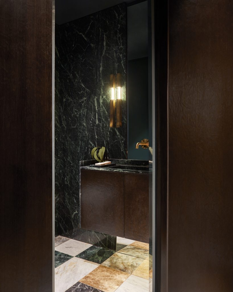 Interior of a bathroom with dark green marble walls and mosaic marble tiling with dark wood features.