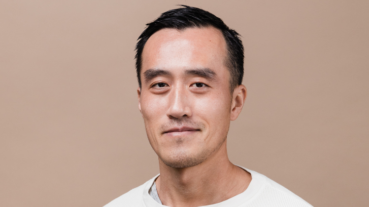 Portrait of Victor Tam smiling in a white sweatshirt against a light brown background