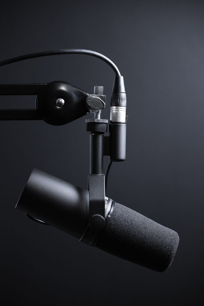 A black microphone suspended from a holster against a black background.