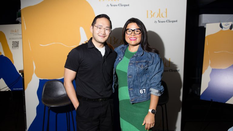 Photo of Editor in Chief of Glory Media, Lance Chung, with Jenn Harper, Founder of Cheekbone Beauty. They are posed together smiling in front of a Veuve Clicquot step and repeat